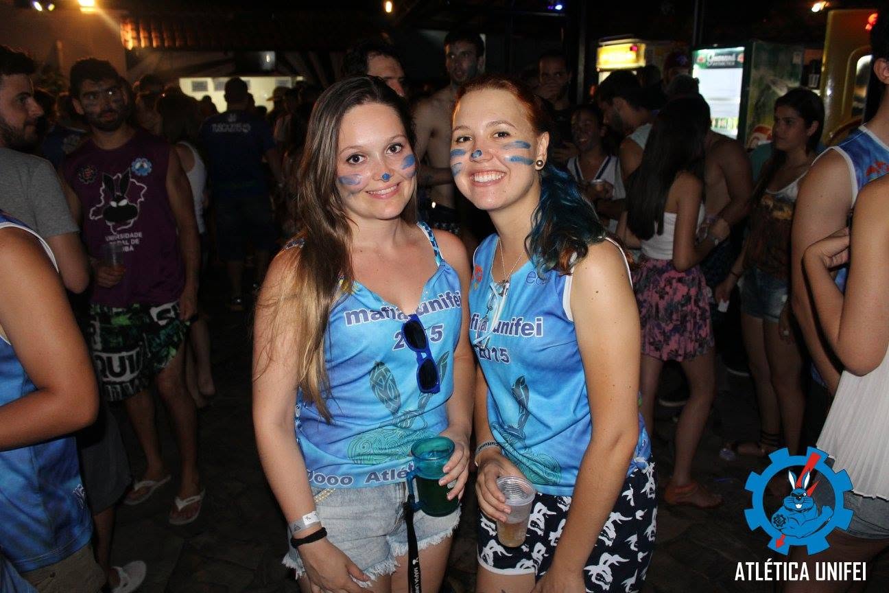 Duas mulheres abraçadas, com pinturas azuis no rosto e camisetas azuis UNIFEI 2015, em confraternização noturna.